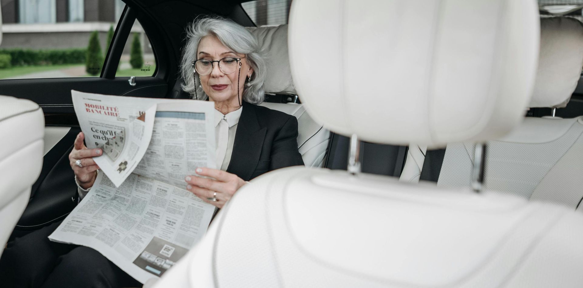 Elderly woman in car reading a newspaper, showcasing a moment of relaxation and focus.
