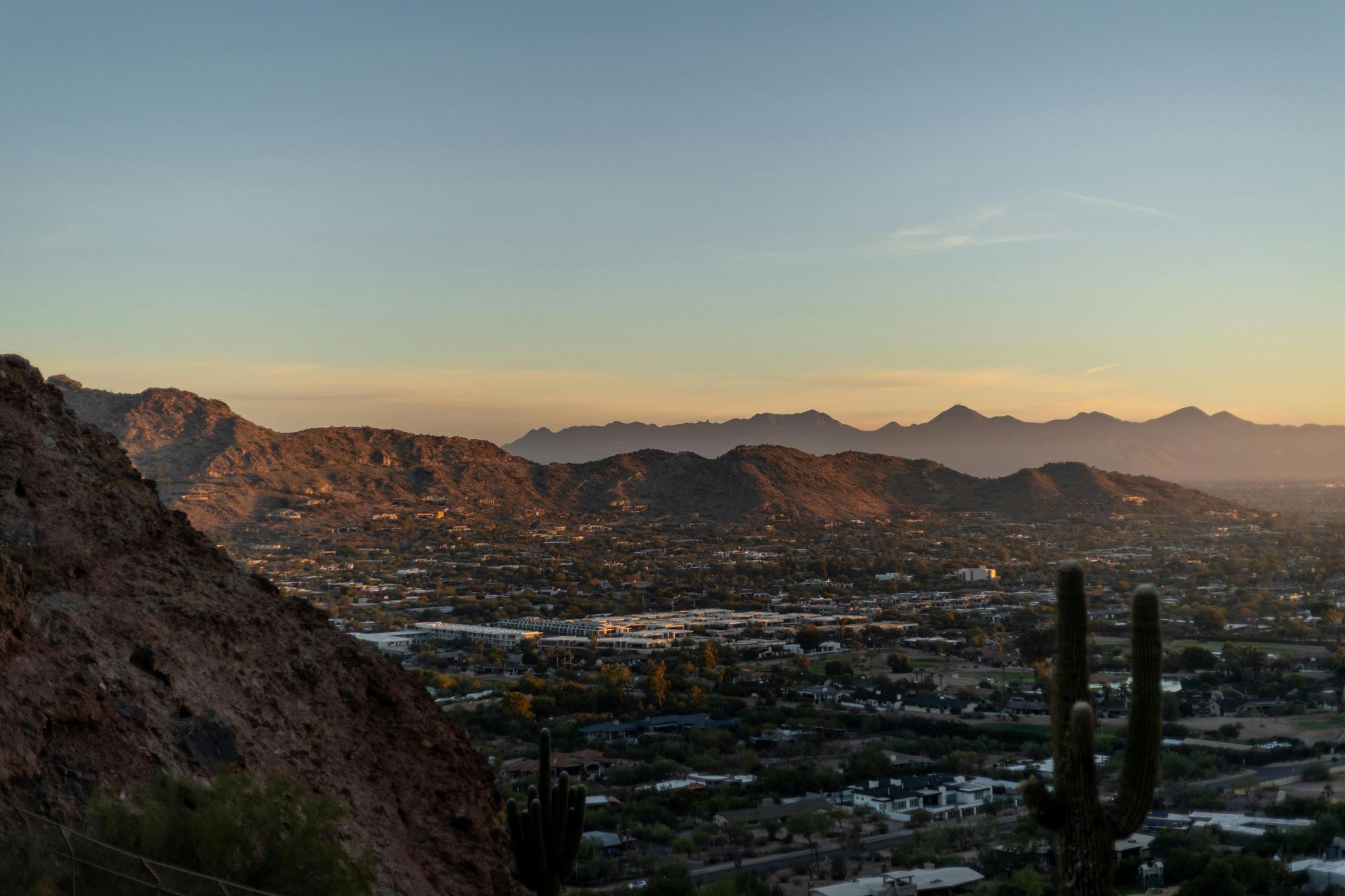 Breathtaking view of Phoenix cityscape and desert mountains at sunset with silhouetted cacti.
